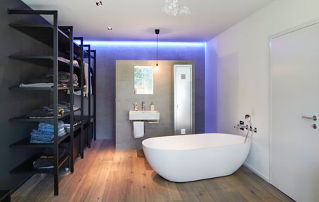 Badezimmer mit Trennwand für Dusche, Toilette und Lavabo mit freistehender Badewanne und farbigem Licht an Hinterwand