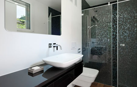 Badezimmer mit dunklen Mosaikplatten und bei Spiegel, Armaturen, Lavabo und Toilette abgerundeten Ecken