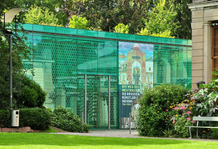 Grüner Glasbau mit markantem Muster, rundherum Garten