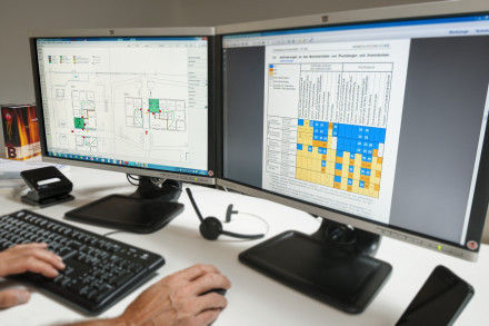 Zwei Bildschirme (links: Grundrissplan, rechts: Brandschutzvorschriften) mit Tastatur