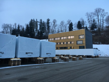 Bürogebäude in Winterstimmung mit auf Palletten-Stapel gelagerte Holzbaumodule davor