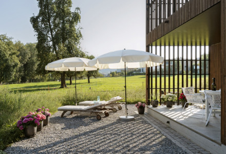 Terrasse mit Kiesbett, mehreren Liegen, Sonnenschirmen und Blumen