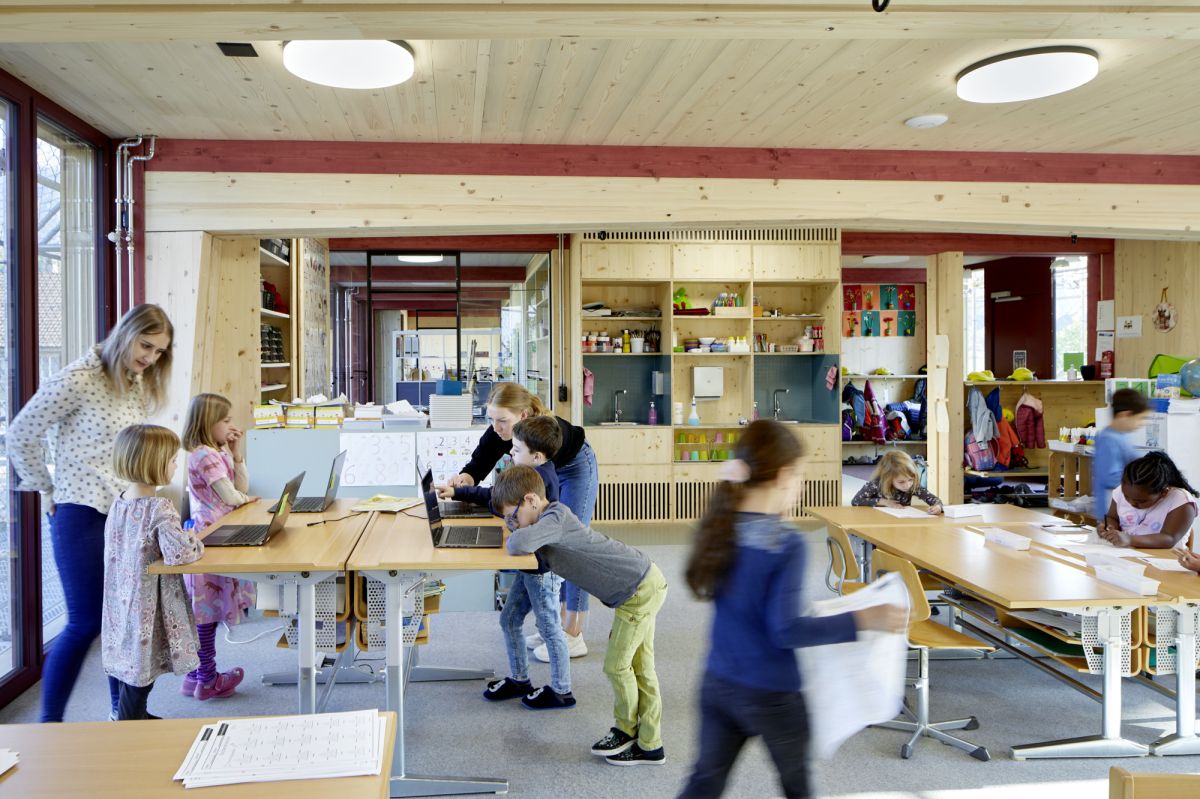 Kinder im Schulzimmer am Lernen mit Papier oder am Laptop.