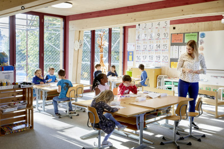 Kinder sitzen an ihren Pulten, lernen oder hören der Lehrerin zu.