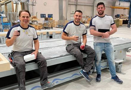 Zwei Zimmermannen sitzend mit Pausengetränke und -essen auf einem Schmetterlingstisch mit ihrem Vorgesetzten stehend