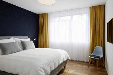 Schlaffzimmer mit Nachdunkler Wandfarbe und goldfarbenen Vorhängen.