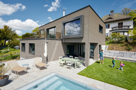 Swimmingpool mit Sitzplatz, Sitzfenster, Terrasse und spielender Familie auf dem Rasen