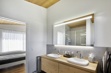Badezimmer mit Holzmöbel und zwei Lavabos mit Blick ins Schlafzimmer