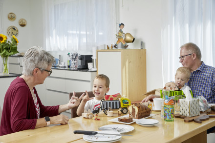 Bauherrschaft mit Enkel am Esstisch beim Essen, im Hintergrund die Küche