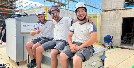 Drei Zimmermänner sitzen auf einer Materialbox auf einer Baustelle während einer Pause