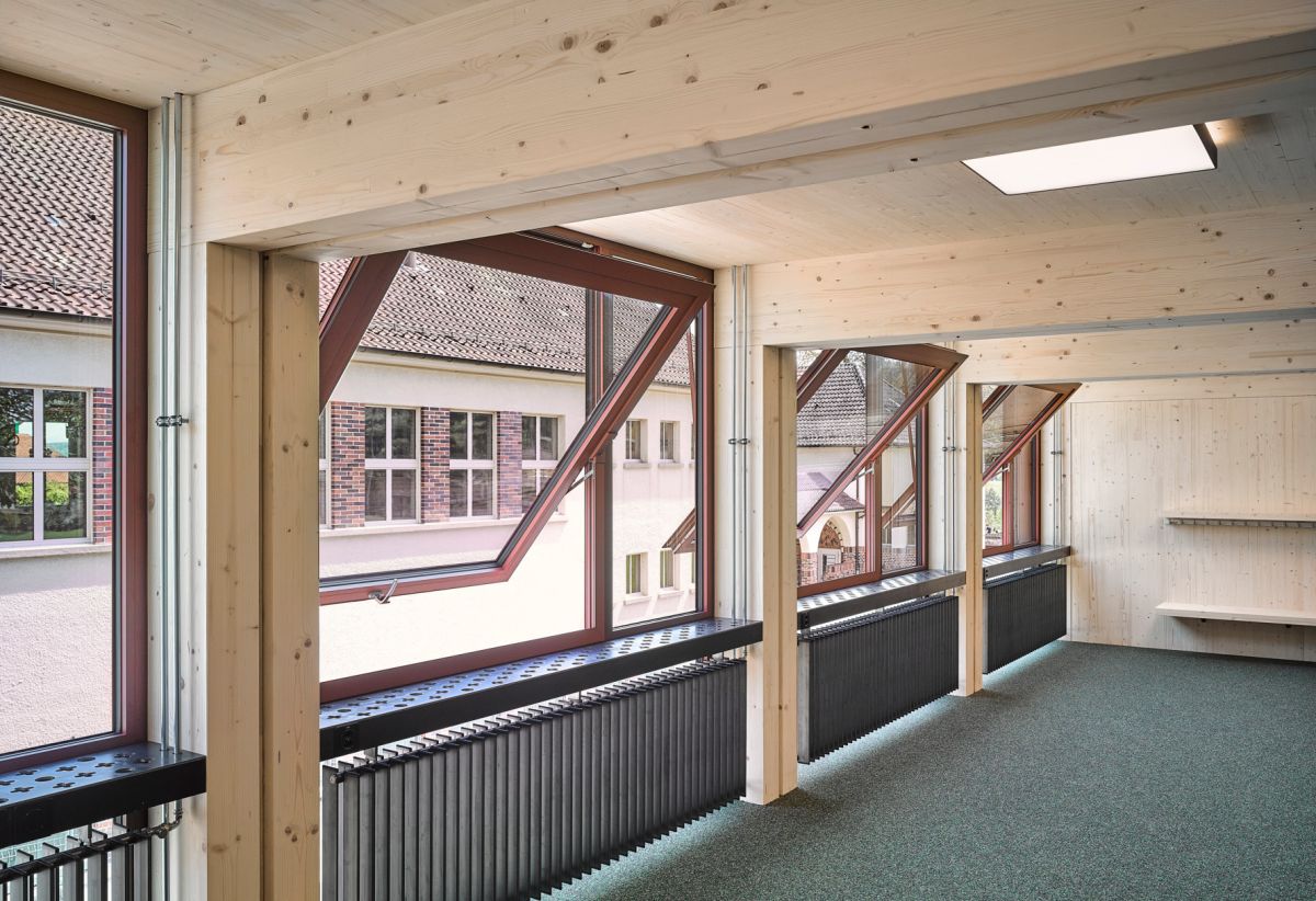 Schulzimmer von innen mit grossen, geöffneten Kippfenstern und viel sichtbarem Holz sowie Heizradiatoren.