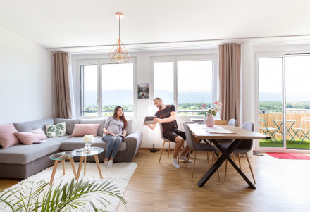Mietende in ihrem modern eingerichteten Wohnzimmer mit Sicht auf den Balkon und den Jura.