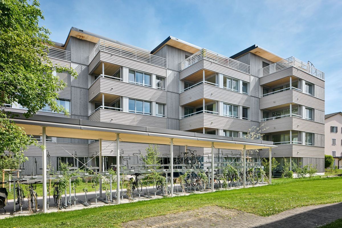 5-geschossiges Mehrfamilienhaus mit Vor- und Rücksprüngen, davor ein grosser, gedeckter Parkplatz für Velos