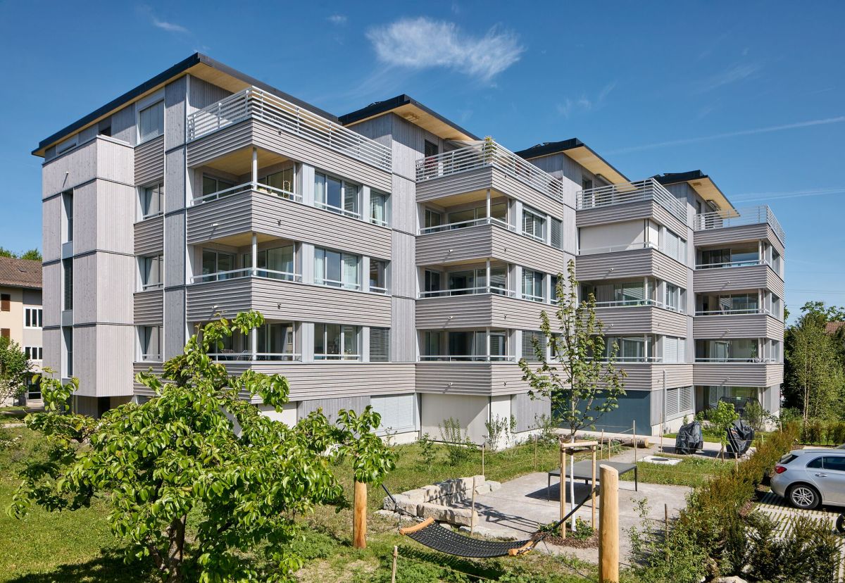 5-geschossiges Mehrfamilienhaus mit Vor- und Rücksprüngen, davor der Gemeinschaftsgarten mit Hängematte, Tisch und Grillstelle