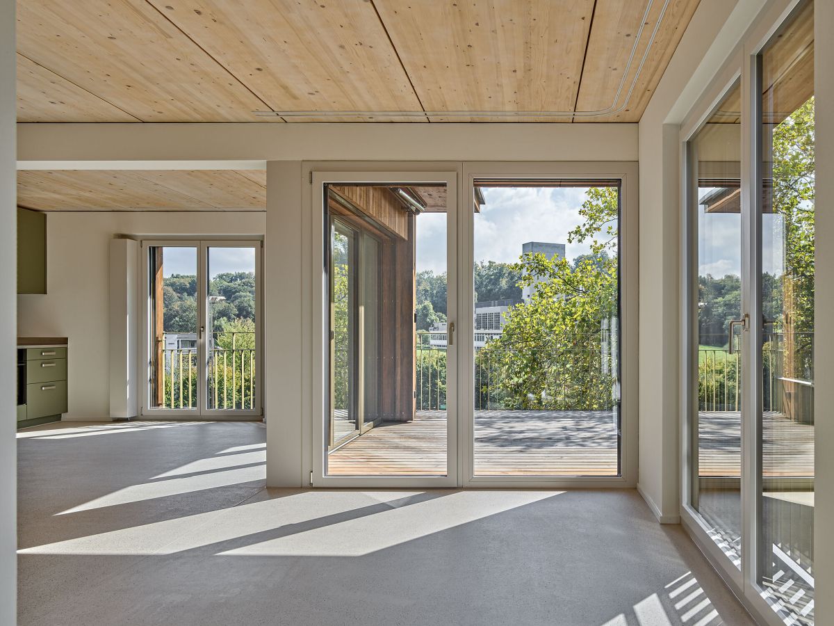 Wohnraum leer, Küche und Essraum links, mit Blick auf den Balkon, sichtbare Holzdecke