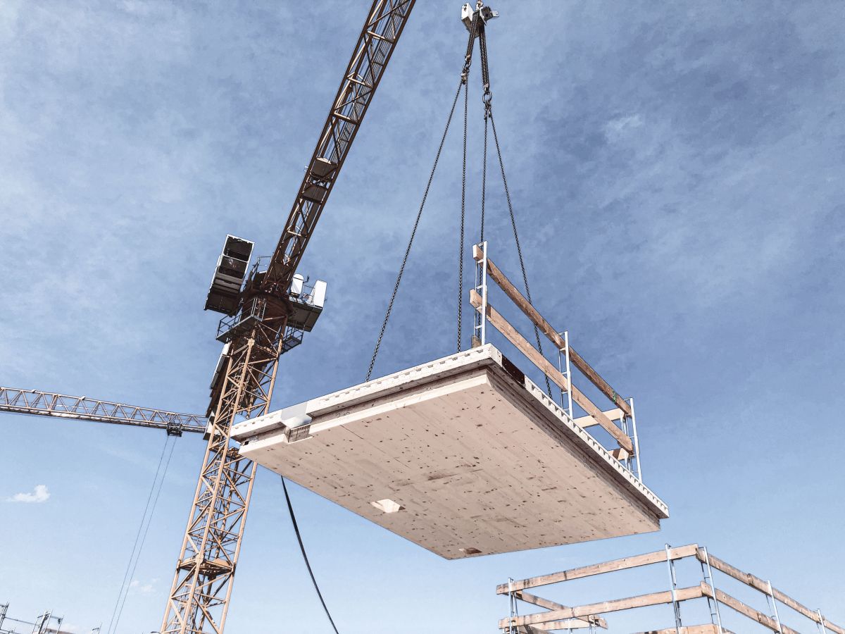 Am Kran schwebendes Holz-Beton-Verbundelement mit Absturzsicherung auf der Baustelle bei der Montage.