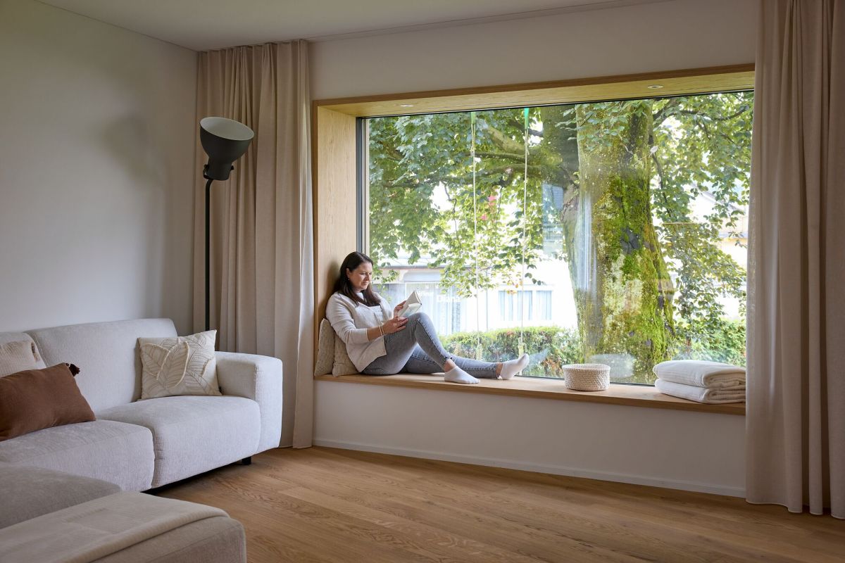 Frau liest sitzend im Sitzfenster mit Blick auf grossen Baum