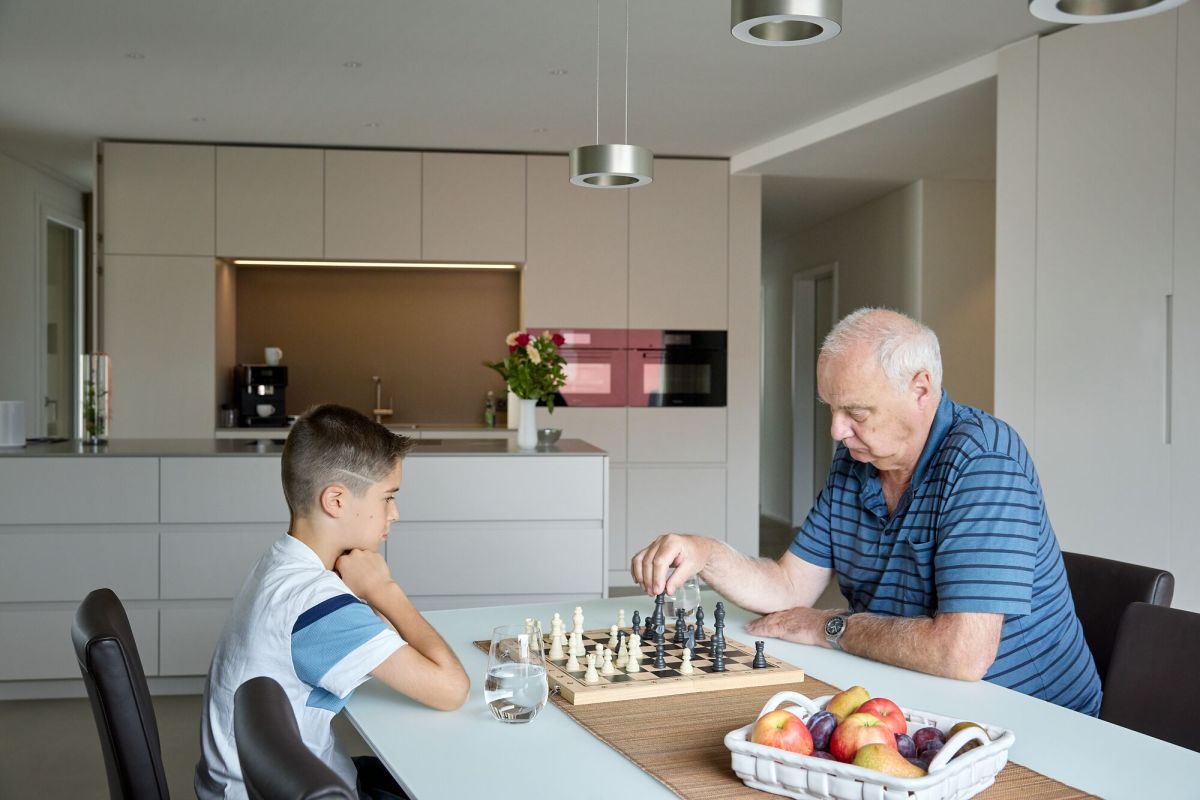 Opa und Enkel beim Schachspielen am Küchentisch, im Hintergrund die Küche mit Kücheninsel