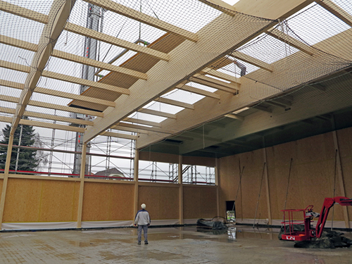 Un élément de plafond est installé dans une salle de gymnastique à 16 mètres au-dessus du sol. Pour garantir la sécurité des charpentiers, un filet est tendu à l’endroit où ils travaillent.