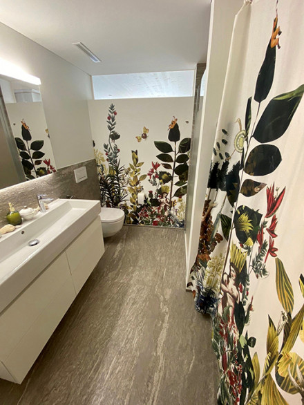 Salle de bains avec rideau de douche représentant des plantes également présentes sur le papier peint.