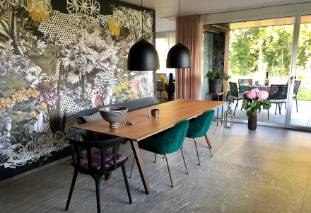 Une table en bois et un papier peint de Rita Krasniqi réalisé à partir d’un collage composé de fleurs, d’animaux et de divers motifs.