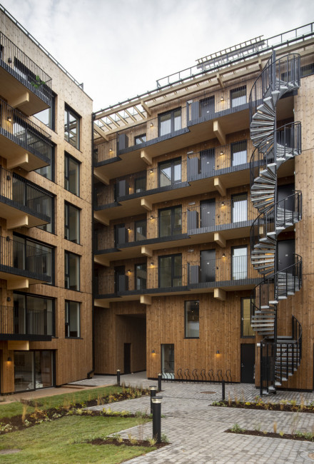 Cour intérieure en ambiance de soirée avec façade en bois et accès par des escaliers et des couloirs extérieurs.