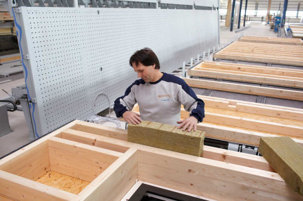 Un collaborateur intègre de la laine minérale comme isolation dans l’ossature bois destinée aux éléments de parois.