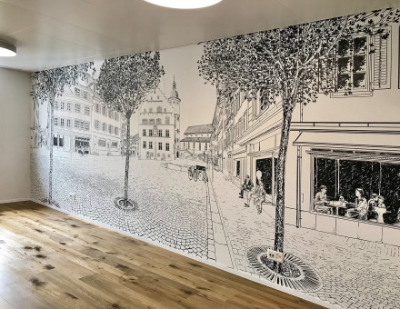 Un mur avec un papier peint réalisé à partir d’un dessin représentant la petite ville de Sursee dans les locaux de la Mobilière.