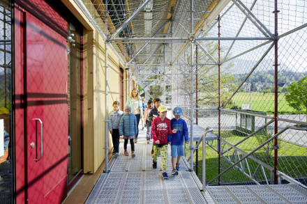 Des enfants empruntent l'escalier extérieur pour rejoindre leur salle de classe, avec l'échafaudage de sécurité tout autour.