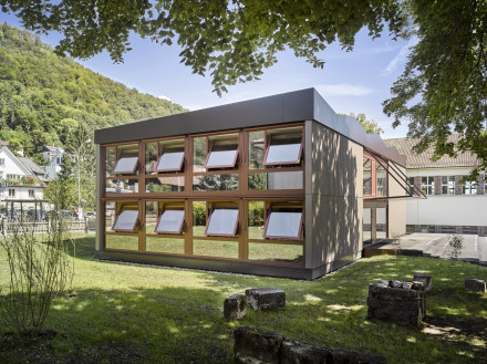 Bâtiment scolaire avec des fenêtres ouvertes. Un côté (ouest) avec fenêtre, un côté (sud) sans fenêtre (entrée).