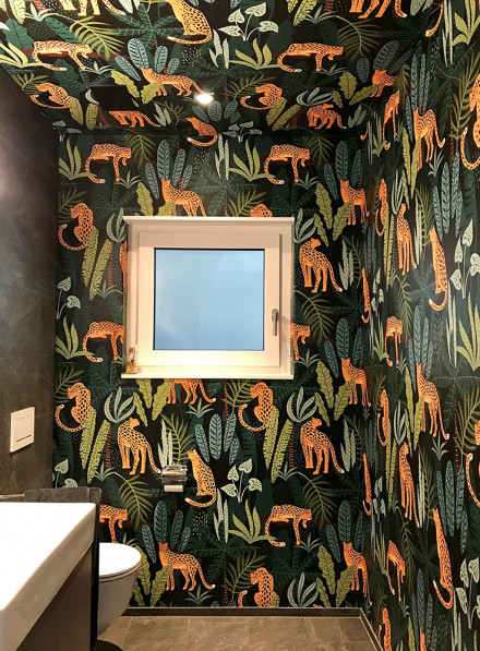 Des toilettes visiteurs avec un papier peint à motif animalier vert, noir et orange.