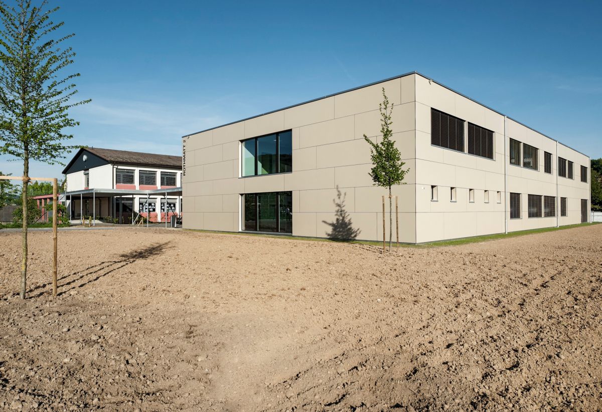 Bâtiment scolaire de deux étages avec deux jeunes arbres.