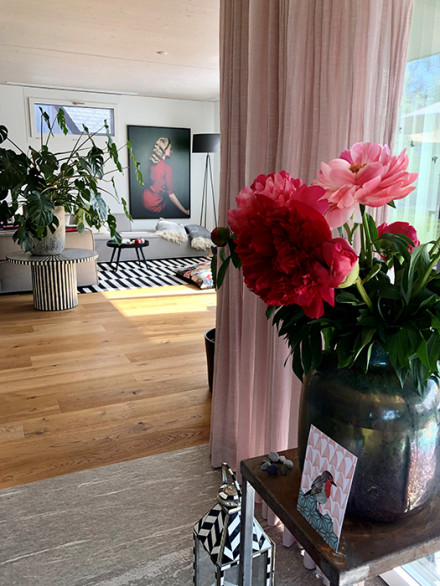 Vue d’ensemble avec un rideau rose poudré, une table en bois au premier plan et un papier peint original.