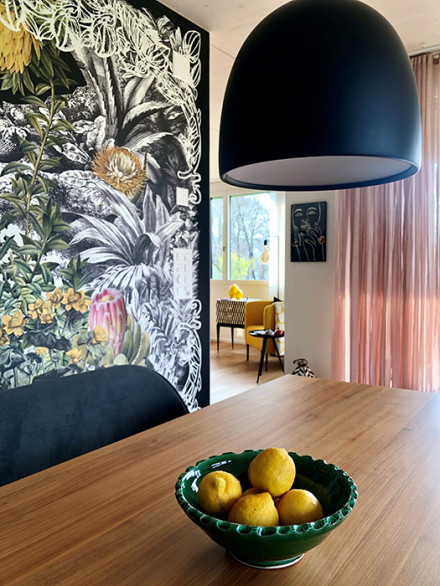 Wohnsituation mit puderfarbenem Vorhang mit Holztisch im Vordergrund und kreativer Wandtapete