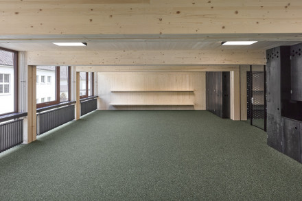 Aula con moquette, travi di legno a vista e soffitto, radiatori e grandi finestre