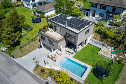 Ripresa da drone della casa unifamiliare con ingresso in garage, giardino, piscina, area di seduta, balcone, finestra di seduta e impianto fotovoltaico.