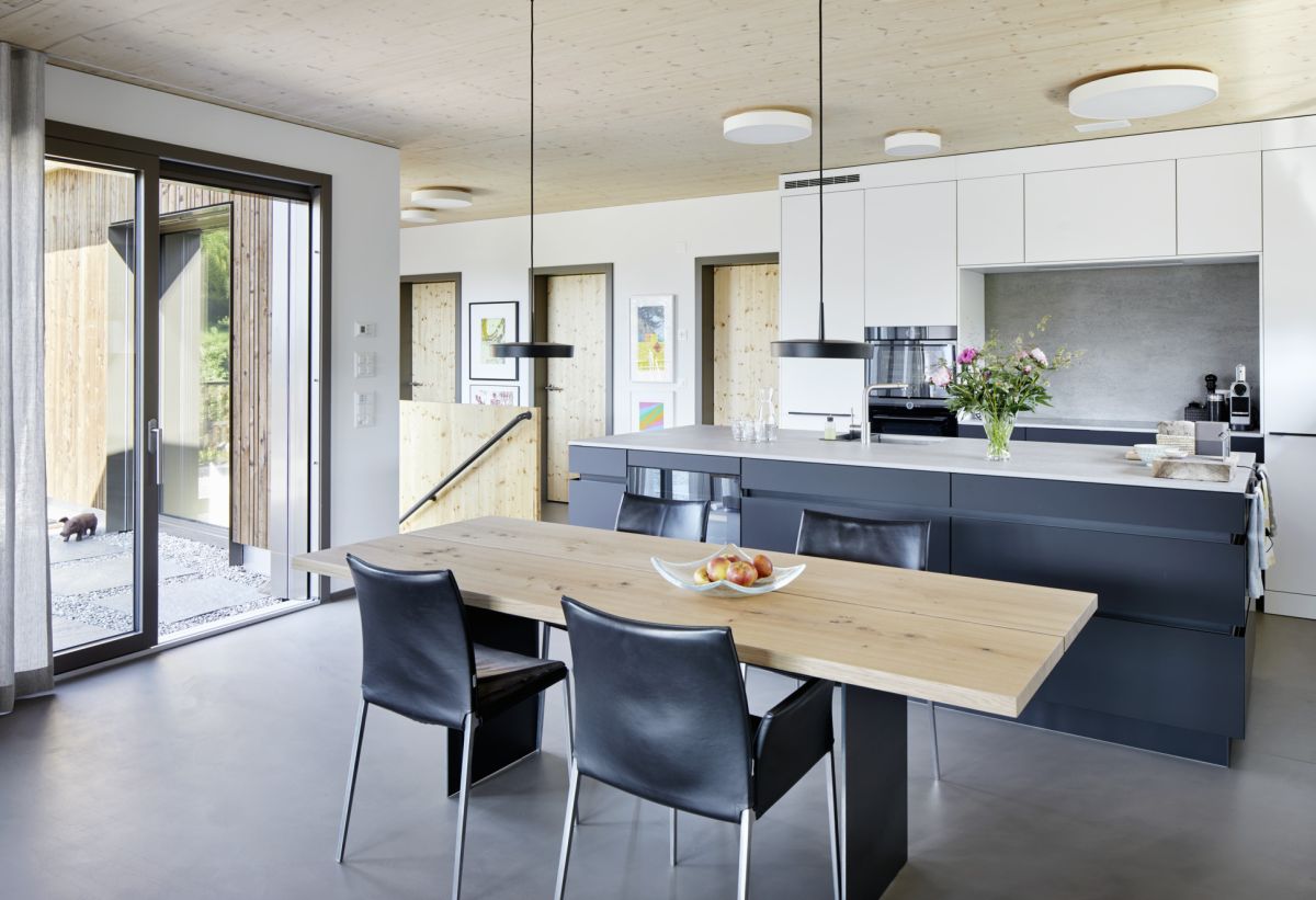 Vue de la table de la salle à manger vers la cuisine ouverte, porte coulissante sur la terrasse et le couloir.