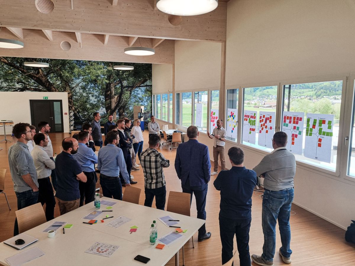 I collaboratori ascoltano un relatore, alle finestre sono appese lavagne a fogli mobili con post-it.